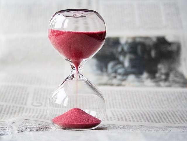 Sanduhr mit rotem Sand vor einer Zeitung 